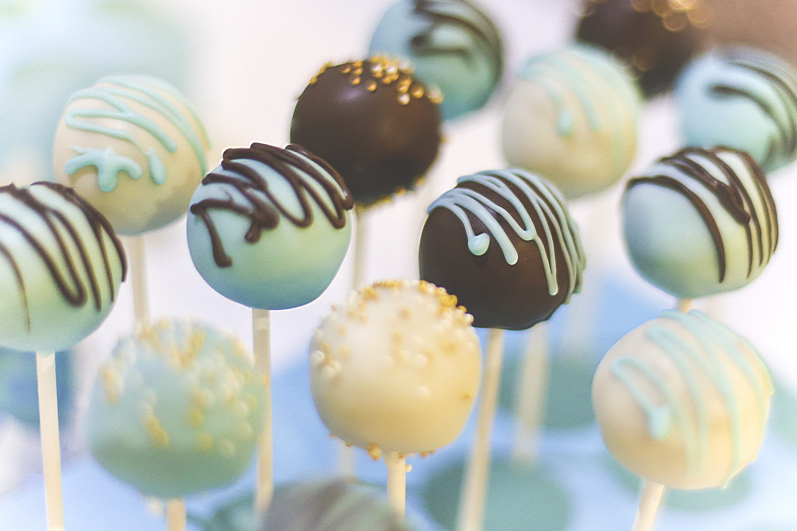 Nahaufnahme verschiedener Cake Pops, einer entzückenden Geschenkidee, dekoriert mit blauen, weißen und schokoladenfarbenen Zuckerguss- und Streuselkuchen auf Stielen.