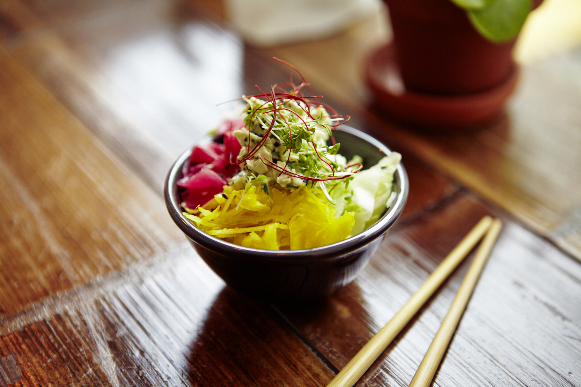 Eine Schüssel bunter Salat mit Kohl und eingelegtem Gemüse steht neben einem Paar Essstäbchen auf einem Holztisch und ist damit die perfekte Geschenkidee für alle, die bunte und gesunde Mahlzeiten lieben.