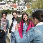 Eine Gruppe von Menschen unterhält sich fröhlich im Freien an einem sonnigen Tag, im Hintergrund sind Häuser zu sehen.