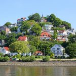 Hangviertel mit farbenfrohen Häusern und üppigem Grün mit Blick auf ein ruhiges Gewässer.