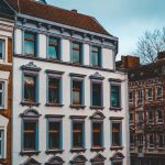 Straßenansicht von Gebäuden im europäischen Stil mit weißen Fassaden und braunen Rahmen unter einem bewölkten Himmel.