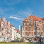 Historische europäische Gebäude mit roten Dächern unter einem klaren blauen Himmel, umgeben von ein paar Bäumen und Zebrastreifenschildern.