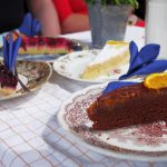 Stücke von Schokoladen-, Beeren- und Sahnekuchen auf Tellern mit dekorativen Servietten auf einer karierten Tischdecke.