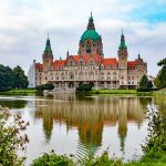 Majestätisches Gebäude mit roten Dächern und Kuppelturm, das sich in einem ruhigen, von Grün umgebenen Teich spiegelt.