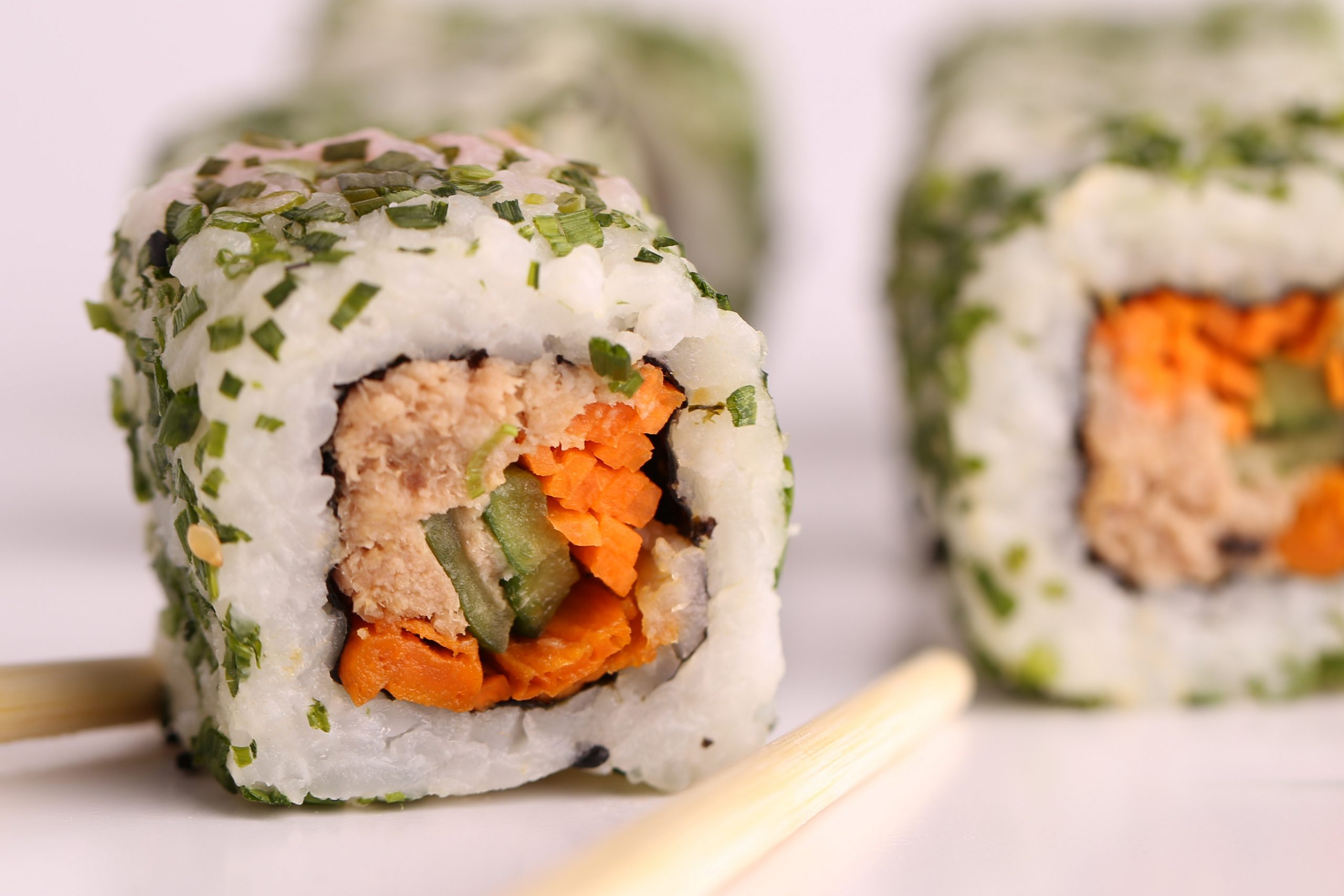 Nahaufnahme von Sushirollen mit Thunfisch-, Karotten- und Gurkenfüllung, garniert mit gehackten Kräutern. Perfekt für ein Junggesellenabschied-Festmahl, diese köstlichen Häppchen werden von Essstäbchen in der Nähe begleitet.