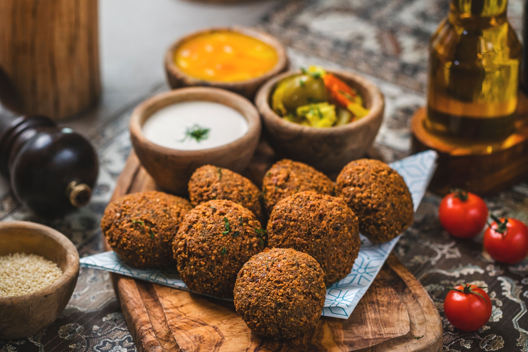 Eine Platte Falafel mit Dip-Saucen, Pickles und Kirschtomaten auf einer dekorativen Tischdecke schafft die perfekte Kulisse für eine lebhafte Junggesellenabschiedsfeier.