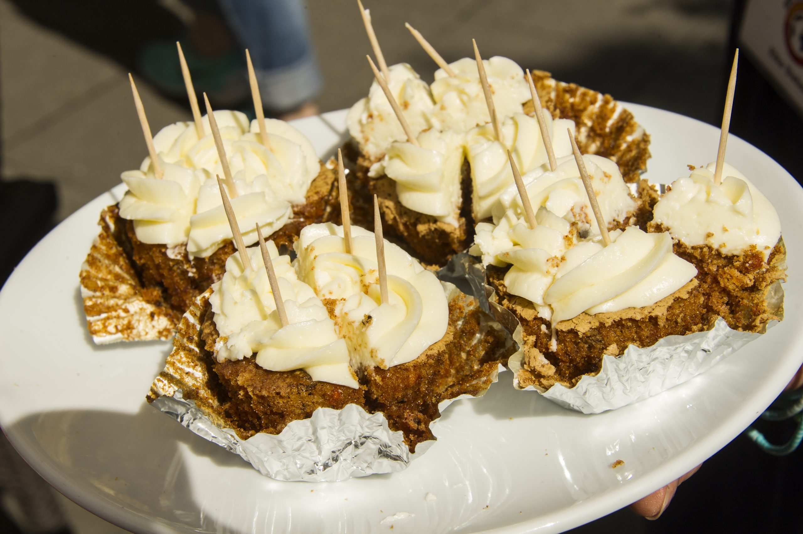 Sechs Stücke Zuckergusskuchen mit Zahnstochern auf einem weißen Teller, jedes in Folie eingewickelt, perfekt für ein Junggesellenabschiedstreffen.