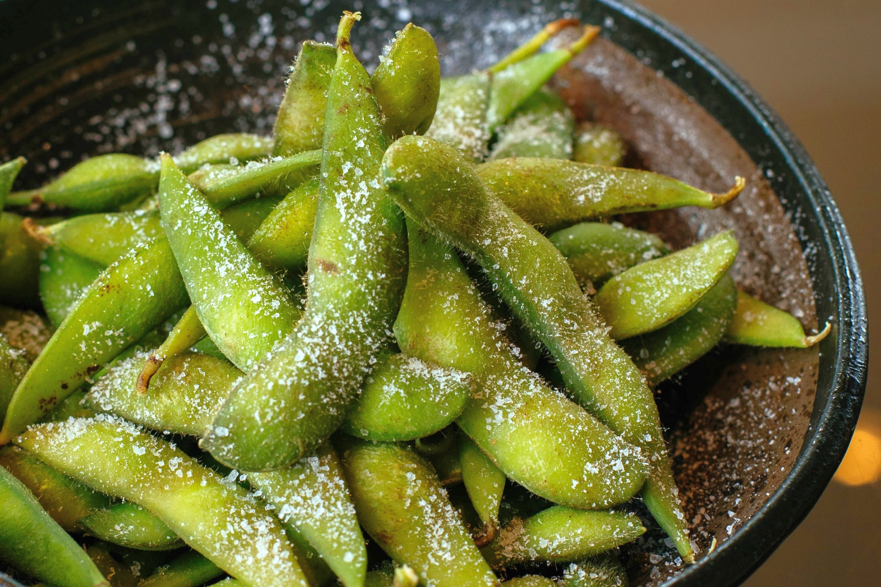 Nahaufnahme von gesalzenen Edamame-Bohnen in einer schwarzen Schüssel, perfekt zum Teilen bei einem Junggesellenabschied, da sie ihre leuchtend grüne Farbe und Textur zur Schau stellen.