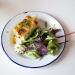 Ein Stück Gemüsequiche mit Beilagensalat auf einem weißen Teller mit blauem Rand, garniert mit Schnittlauch, verleiht dem Junggesellenabschied eine elegante Note.