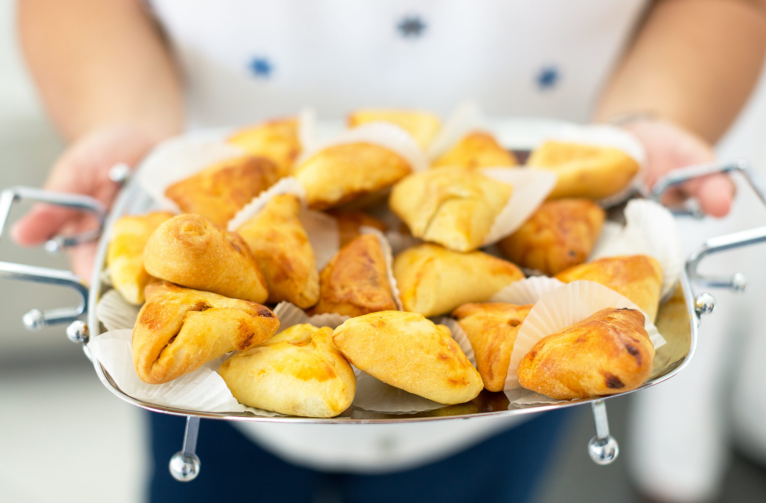 Bei einem lebhaften Junggesellenabschied hält jemand stolz ein Tablett mit frisch gebackenen Empanadas hoch, einige davon in Papierförmchen eingebettet.