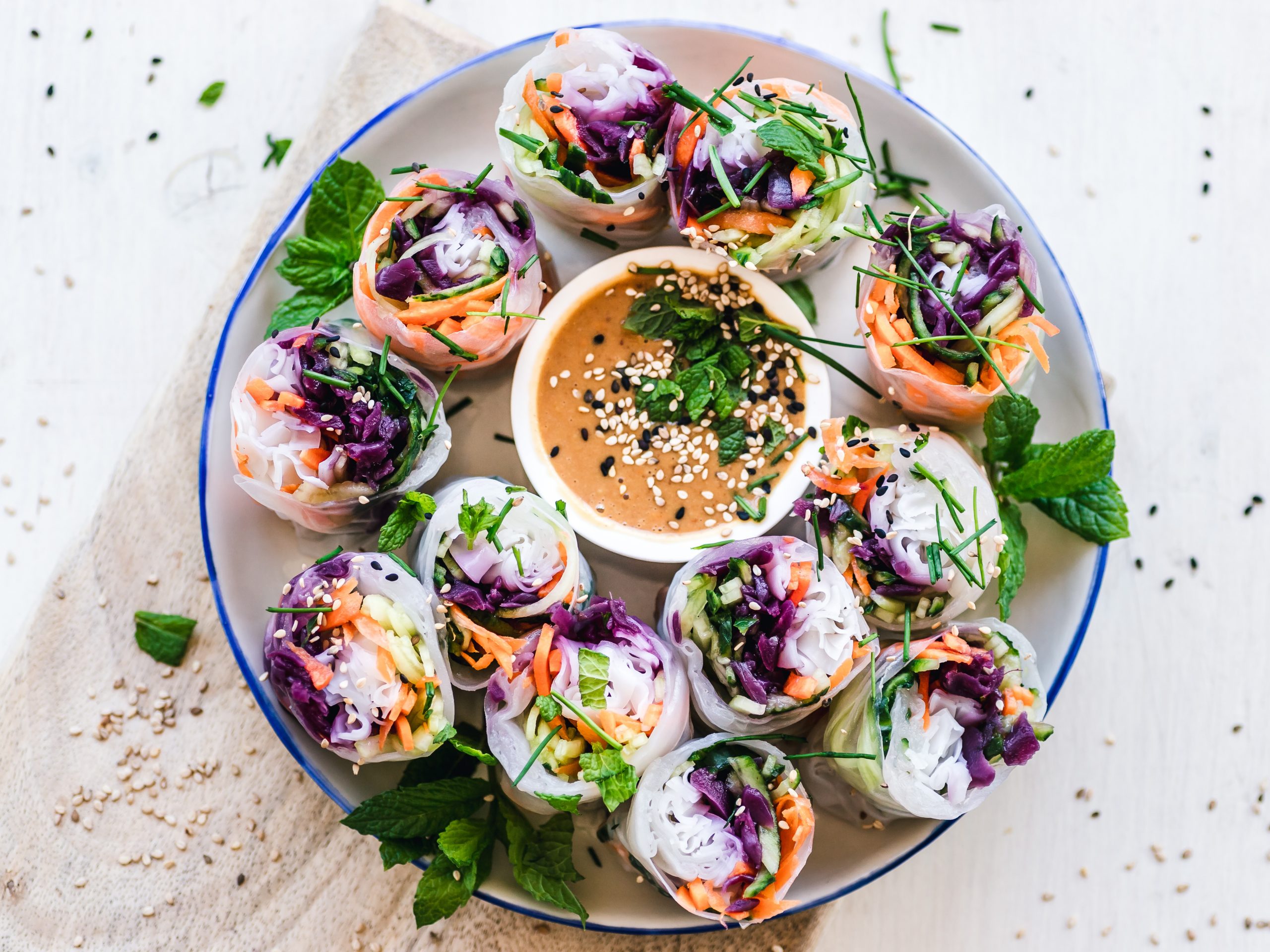 Bunte Gemüse-Frühlingsrollen um eine Schale mit Dip-Sauce herum angeordnet, perfekt für einen lebhaften Junggesellenabschied, garniert mit Kräutern und Sesamkörnern.