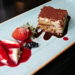 Tiramisu mit Erdbeeren, Beeren und Soße auf einem blauen rechteckigen Teller.