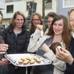 Eine Gruppe von Menschen lächelt und hält im Freien ein Tablett mit kleinen Desserts.