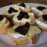 Mit Käse und dunkler Fruchtmarmelade belegte Brotscheiben auf einem weißen Teller.