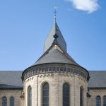 Steinkirche mit Rundtürmen und spitzen Kirchtürmen vor einem klaren blauen Himmel, eingebettet im pulsierenden Kölner Stadtteil Sülz.