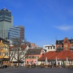 Ein Stadtplatz mit farbenfrohen historischen Gebäuden und modernen Hochhäusern unter einem klaren blauen Himmel.