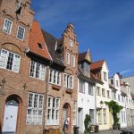 Eine Reihe farbenfroher, historischer Backstein- und Stuckhäuser unter einem klaren blauen Himmel.