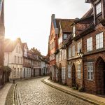 Sonnenbeschienene Kopfsteinpflasterstraße mit charmanten Backsteinhäusern, gewölbten Türen und weiß gerahmten Fenstern.