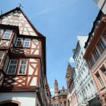 Straßenansicht mit traditionellen Fachwerkhäusern und einer entfernten Kathedrale unter einem klaren blauen Himmel.