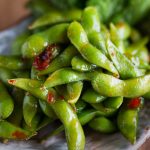 Eine Schüssel gedämpfte Edamame, überzogen mit Chilisauce auf einem Holztisch.