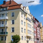 Farbenfrohe historische Gebäude unter einem blauen Himmel mit vereinzelten Wolken, aufgereiht entlang einer Straße.