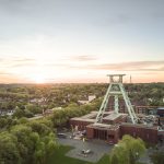 Luftaufnahme der Kohlezeche Zollverein, umgeben von Bäumen, unter einem Sonnenuntergangshimmel.