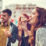 Eine Gruppe von Freunden genießt Pizzastücke im Freien in einer Stadt.