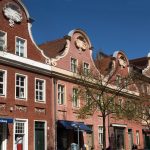 Historische Gebäude aus rotem Backstein mit reich verzierten Satteldächern unter einem klaren blauen Himmel.