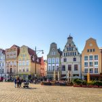 Lebhafter Stadtplatz mit farbenfrohen Gebäuden und Menschen, die an einem sonnigen Tag spazieren gehen.