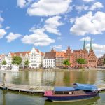 Panoramablick auf traditionelle Gebäude an einem Fluss mit Booten unter einem blauen Himmel mit flauschigen Wolken.