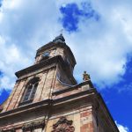 Niedrige Ansicht eines historischen Kirchturms vor einem strahlend blauen Himmel mit flauschigen Wolken.