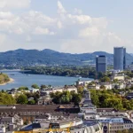 Panoramablick auf Bonn, Deutschland mit dem Rhein, umgeben von Gebäuden und Hügeln in der Ferne unter einem blauen Himmel.