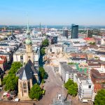 Luftaufnahme einer Stadtlandschaft mit einer Kirche, modernen Gebäuden und Grünflächen an einem klaren Tag.