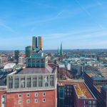 Luftaufnahme der Dortmunder Stadtlandschaft mit städtischen Gebäuden und dem ikonischen U-Turm, der stolz unter einem klaren blauen Himmel steht.