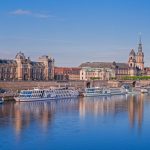 Malerische Aussicht auf die Skyline von Dresden mit historischen Gebäuden und ankernden Booten entlang der Elbe unter einem klaren blauen Himmel, die die reiche Kultur der Stadt präsentiert und Touristen anzieht.