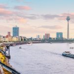 Genießen Sie einen atemberaubenden Panoramablick auf Düsseldorf, wo der majestätische Rhein das Stadtbild durchzieht. Bewundern Sie die Mischung aus modernen und historischen Gebäuden, gekrönt vom ikonischen Rheinturm, der sich anmutig unter einem teilweise bewölkten Himmel erhebt.