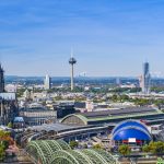 Luftaufnahme von Köln mit Dom, Fernsehturm, Bahnhof und Rheinbrücke an einem klaren Tag.