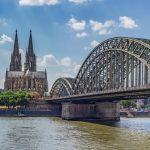 Panoramablick auf eine große Stahlbrücke über einen Fluss mit einer Kathedrale und einer Stadtlandschaft im Hintergrund.