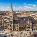 Luftaufnahme des Münchner Marienplatzes mit Neuem Rathaus und Frauenkirche unter blauem Himmel.