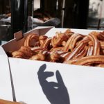 Schachtel gezuckerte Churros mit einem verspielten Handschatten im Sonnenlicht.