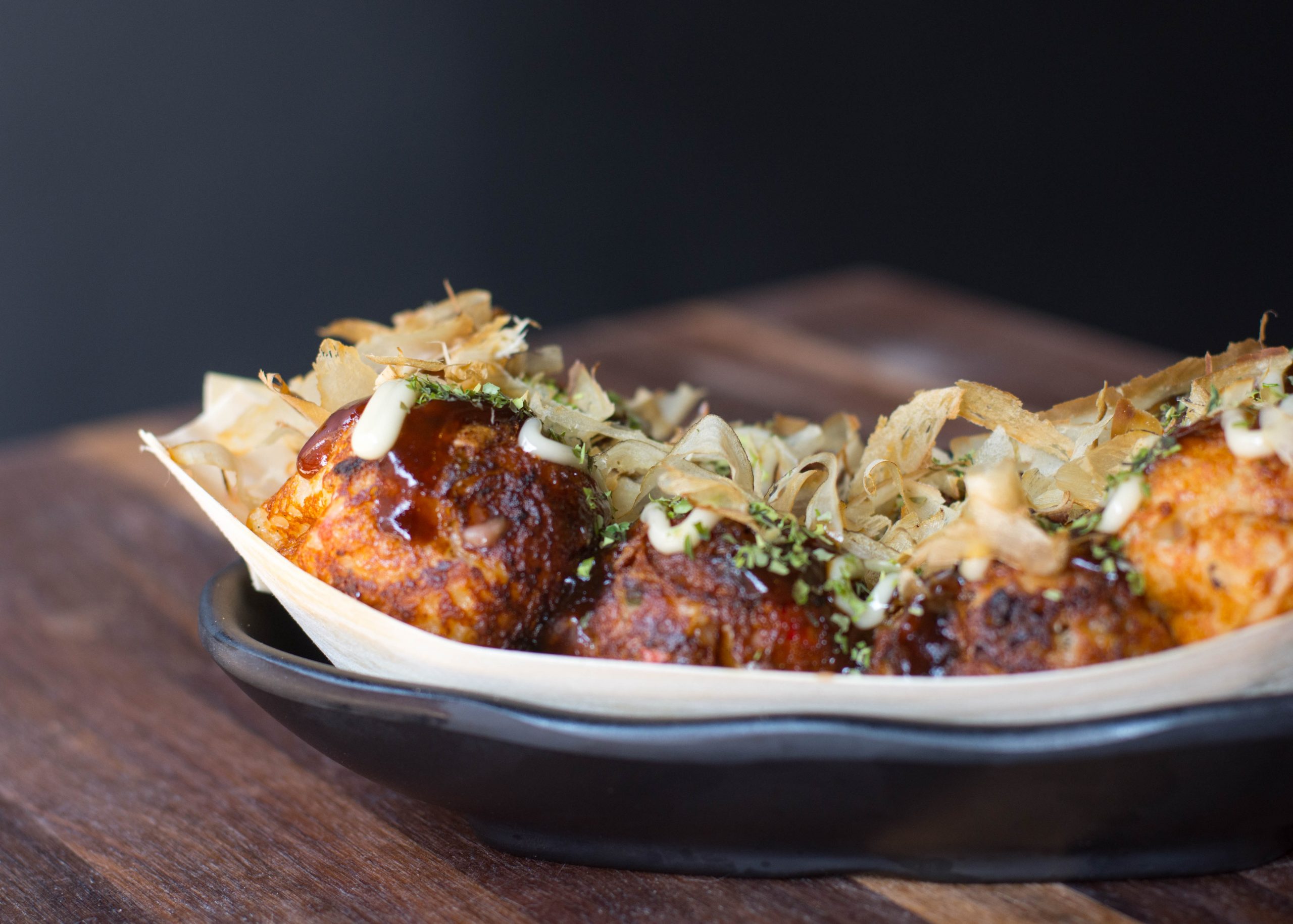 Takoyaki serviert auf einem schwarzen Teller mit festlichem Belag, perfekt für eine Weihnachtsfeier, elegant präsentiert auf einem Holztisch.