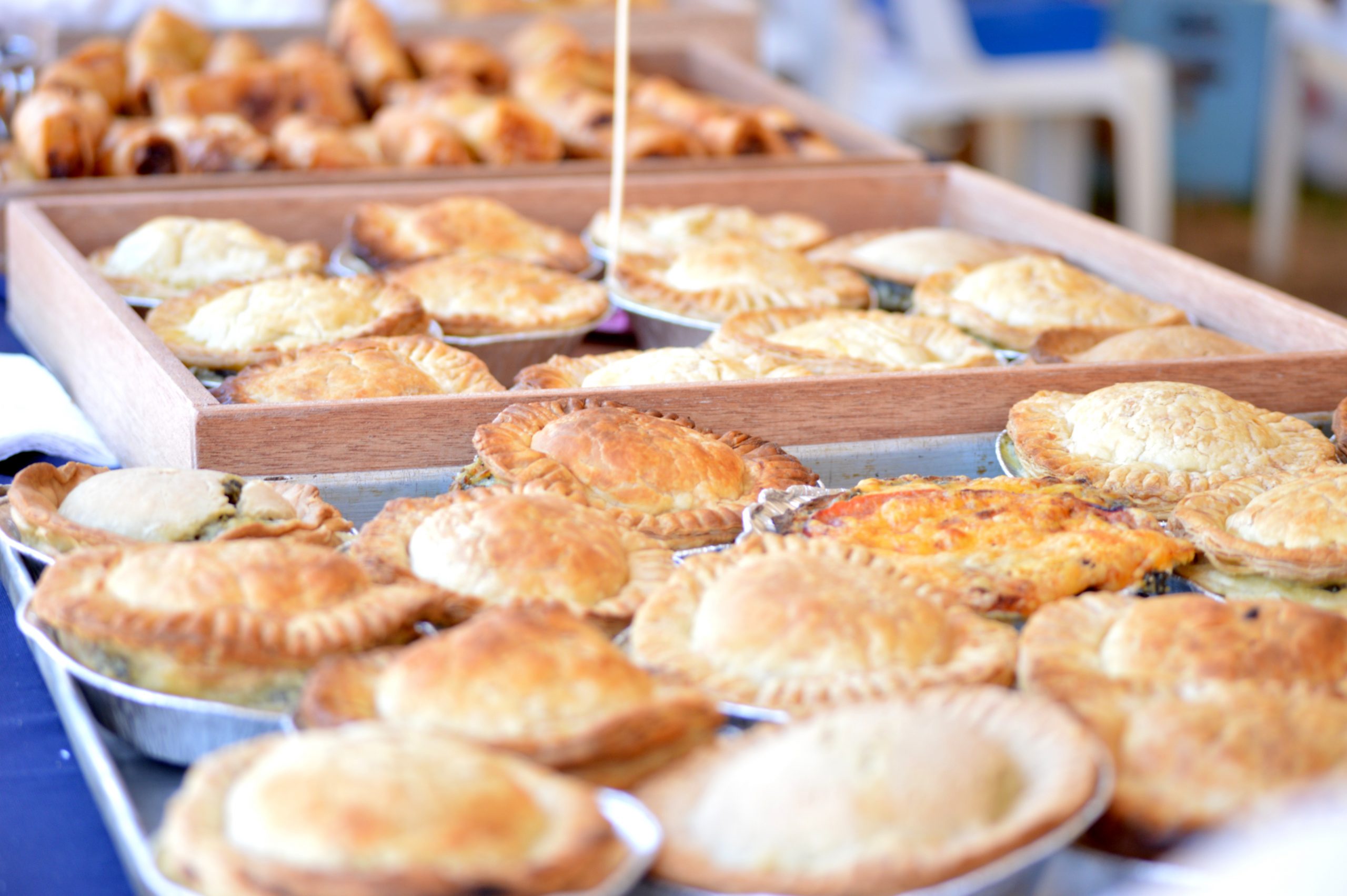 Eine Auswahl an frisch gebackenen Kuchen und Gebäck, perfekt für eine Weihnachtsfeier, werden an einem geschäftigen Marktstand hübsch auf Holztabletts präsentiert.