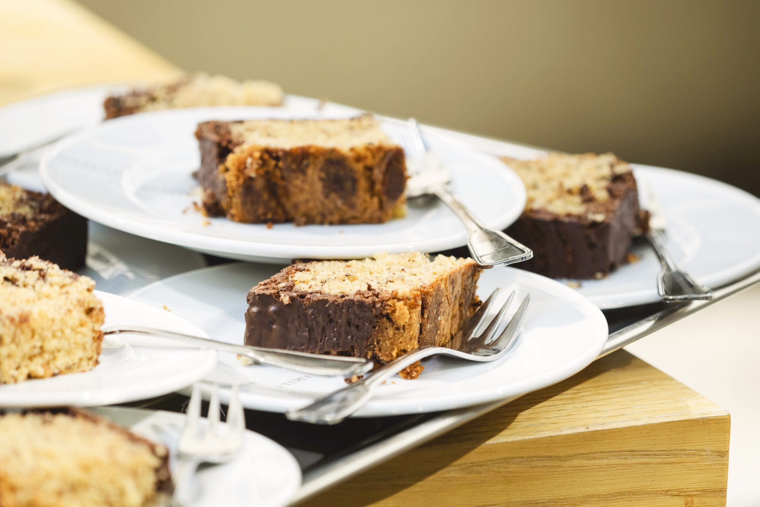 Kuchenstücke mit Schokoladenglasur auf weißen Tellern, jeweils mit einer Gabel versehen, zieren den Holztisch und fangen die festliche Stimmung einer Weihnachtsfeier perfekt ein.