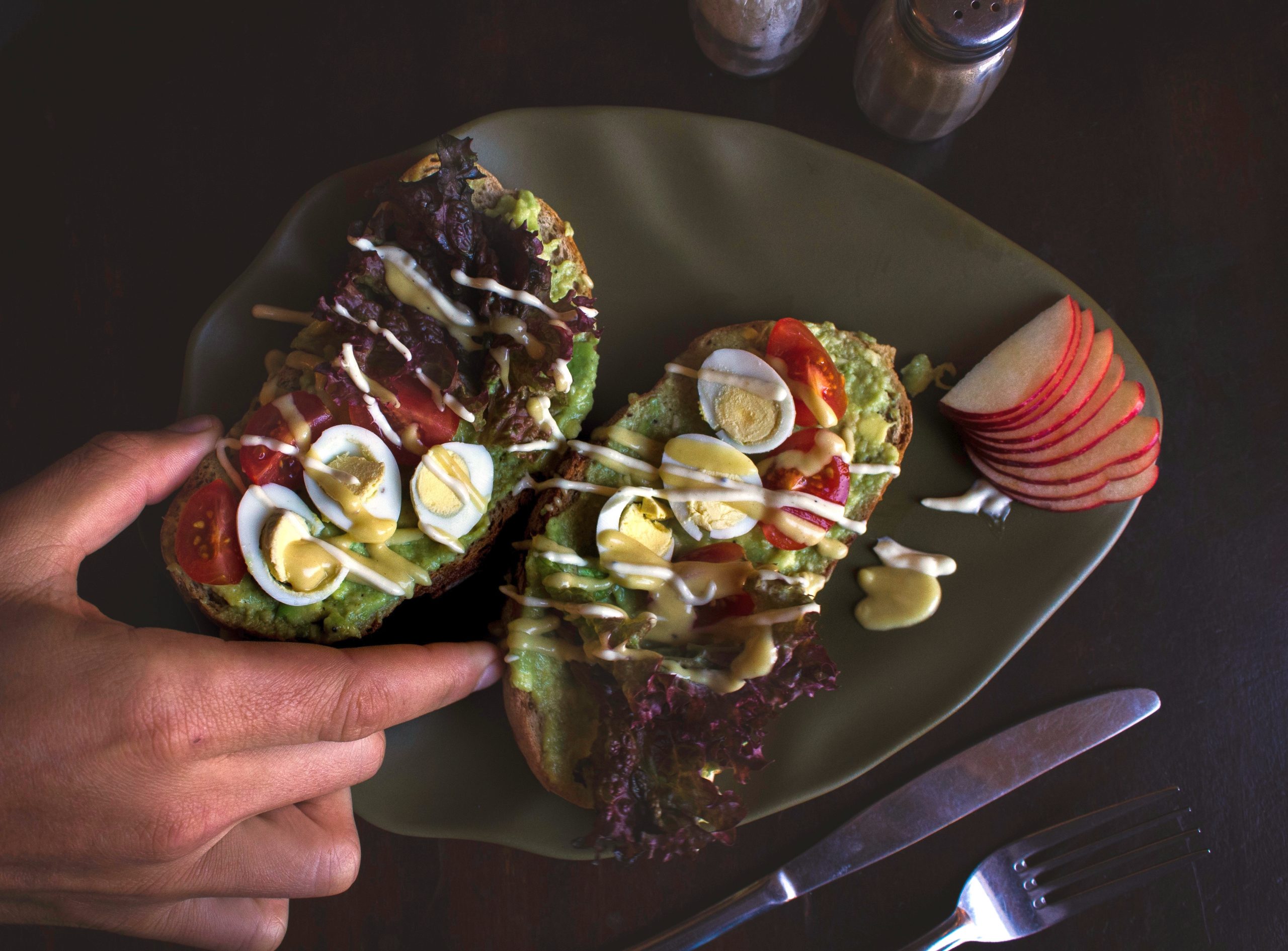 Verwöhnen Sie sich bei einer festlichen Weihnachtsfeier mit einem kunstvollen Teller mit handgehaltenem Avocado-Toast, belegt mit Eiern, Tomaten, einer köstlichen Glasur und knusprigen Apfelscheiben.