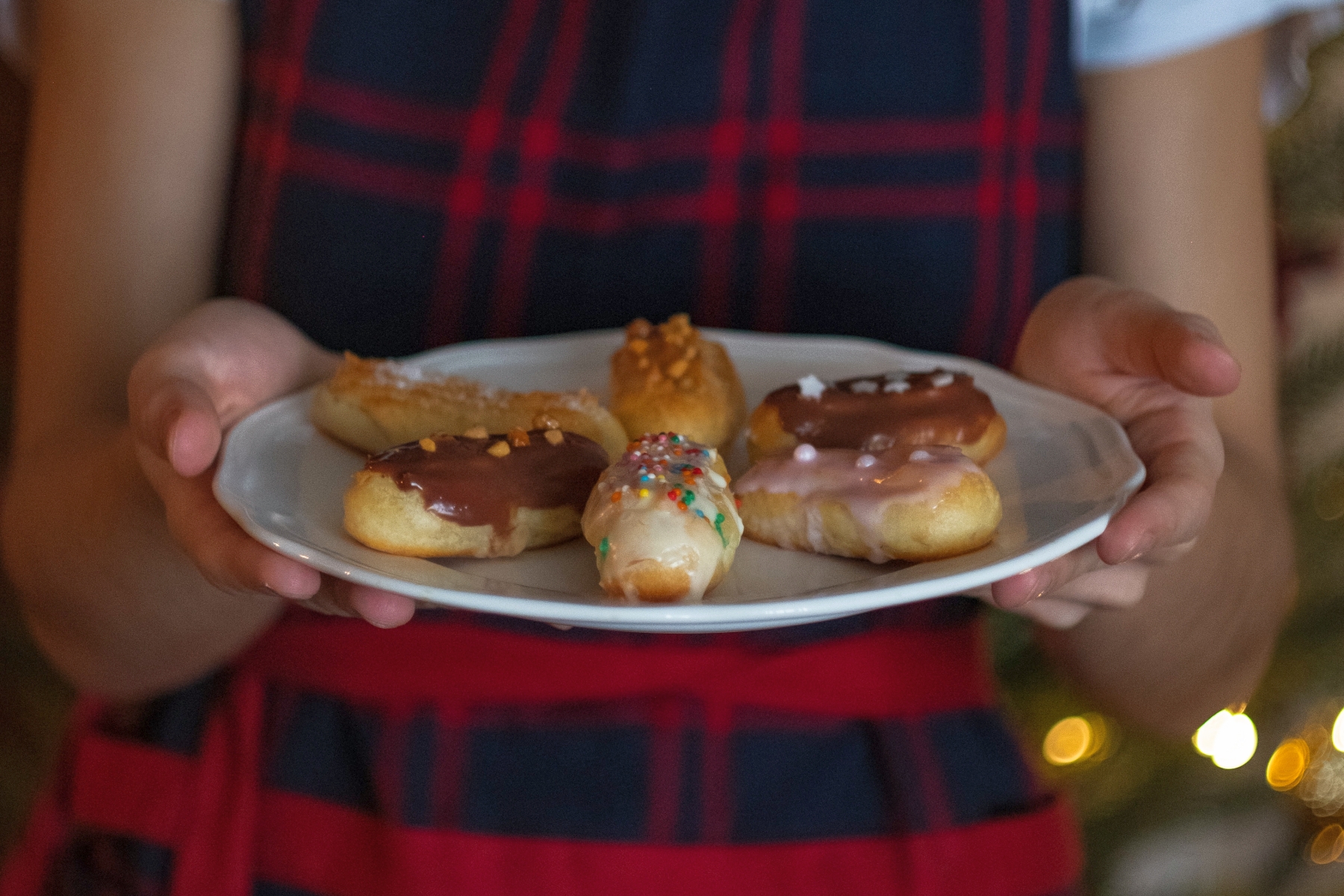 Bei einer festlichen Weihnachtsfeier hält jemand stolz einen Teller mit verschiedenen glasierten Eclairs, verziert mit bunten Streuseln und köstlichen Toppings.