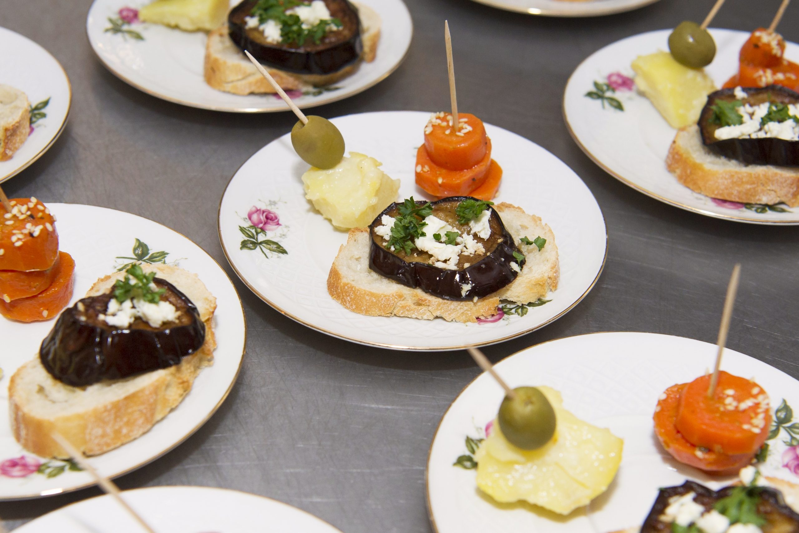 Teller mit verschiedenen Canapés, perfekt für eine Weihnachtsfeier, darunter Auberginen auf Brot und Spieße, garniert mit Oliven, Käse und Tomatenscheiben.