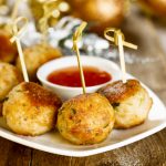 Fleischbällchen am Spieß mit Dip-Sauce auf einem weißen Teller serviert, perfekt für eine festliche Weihnachtsfeier auf einem rustikalen Holztisch.