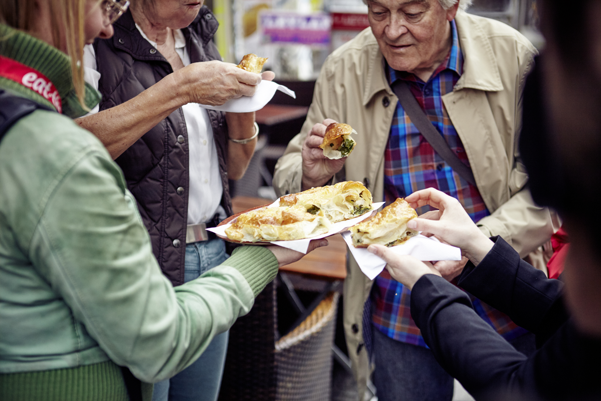 Eine Gruppe von Menschen in Duisburg genießt Gebäck im Freien, teilt sich Teller mit gefülltem Brot und diskutiert über mögliche Nebenjobs.