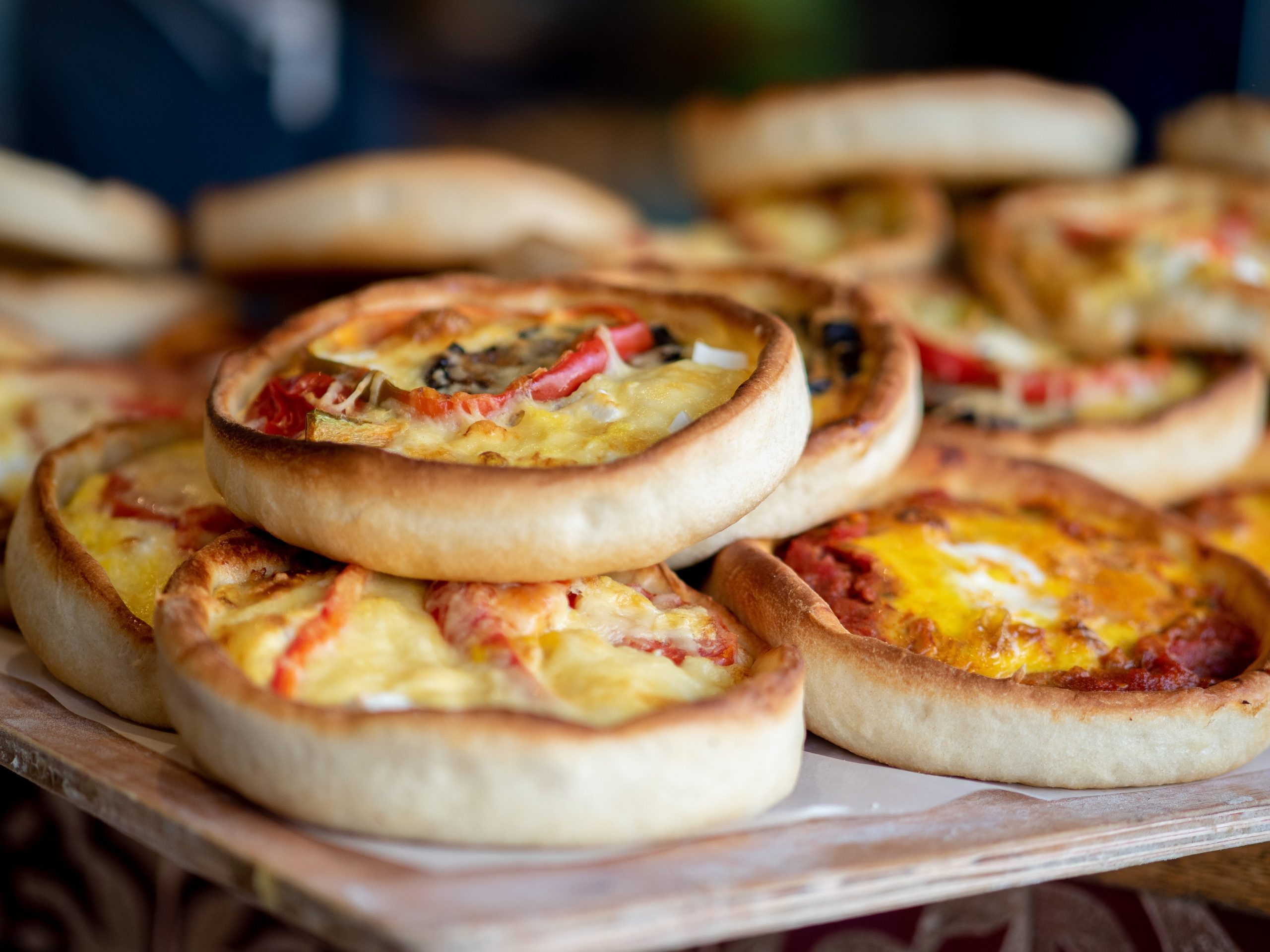 Ein Stapel bunter Mini-Pizzen mit verschiedenen Belägen auf einem Holztablett, perfekt zum Teilen bei einem Betriebsausflug.