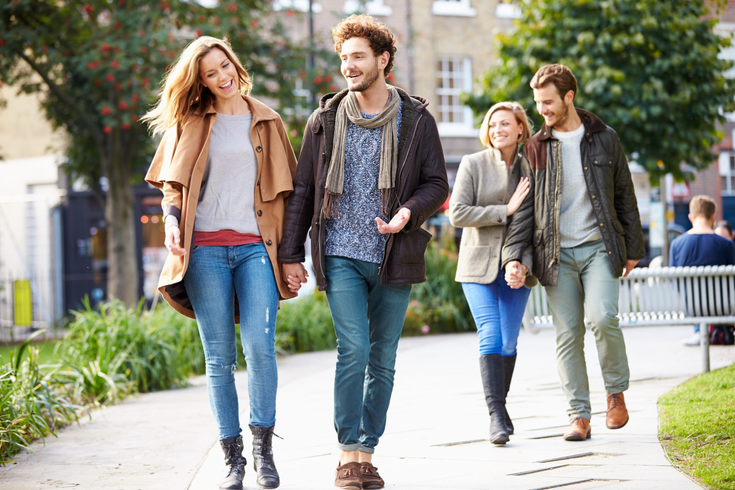 Zwei vor Freude sprühende Paare spazieren an einem sonnigen Tag gemeinsam durch den Park – eine perfekte Kulisse, um eine unvergessliche Geschenkidee festzuhalten.